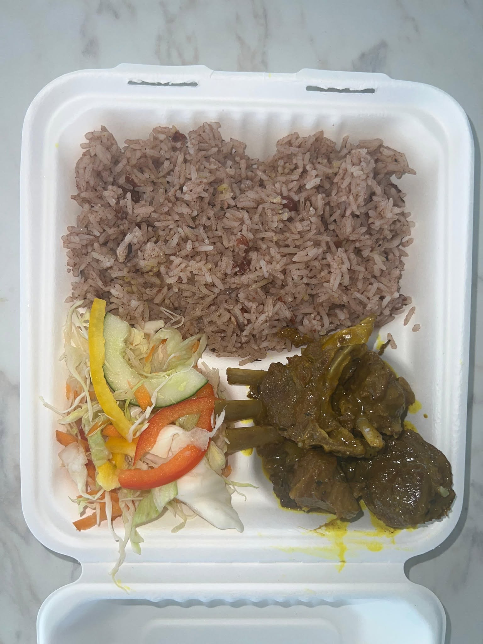 A real takeaway plate of curry goat with rice and peas